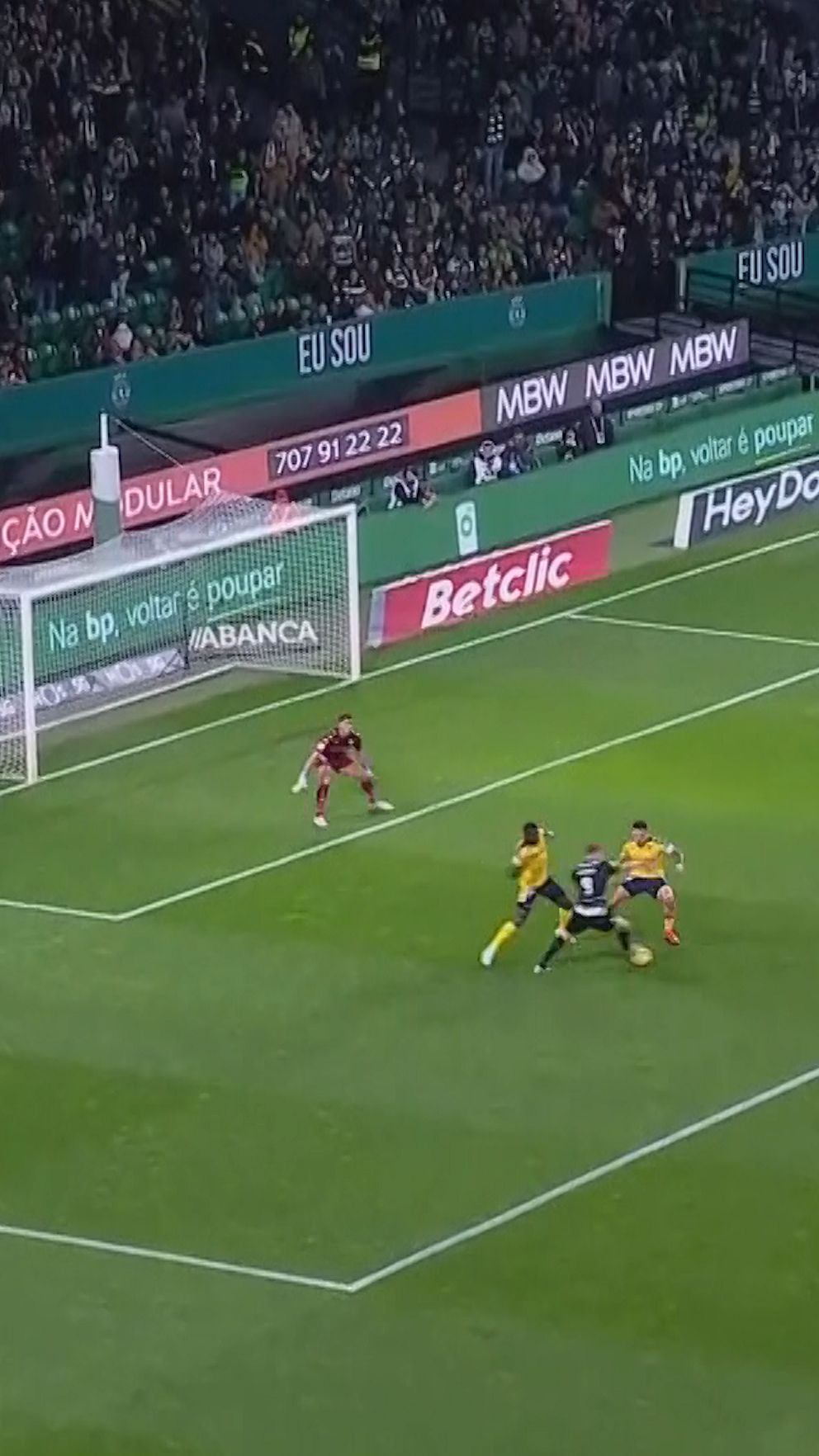 Fotbollsspelare försöker göra mål, målvakt förbereder räddning inför publik på läktaren.