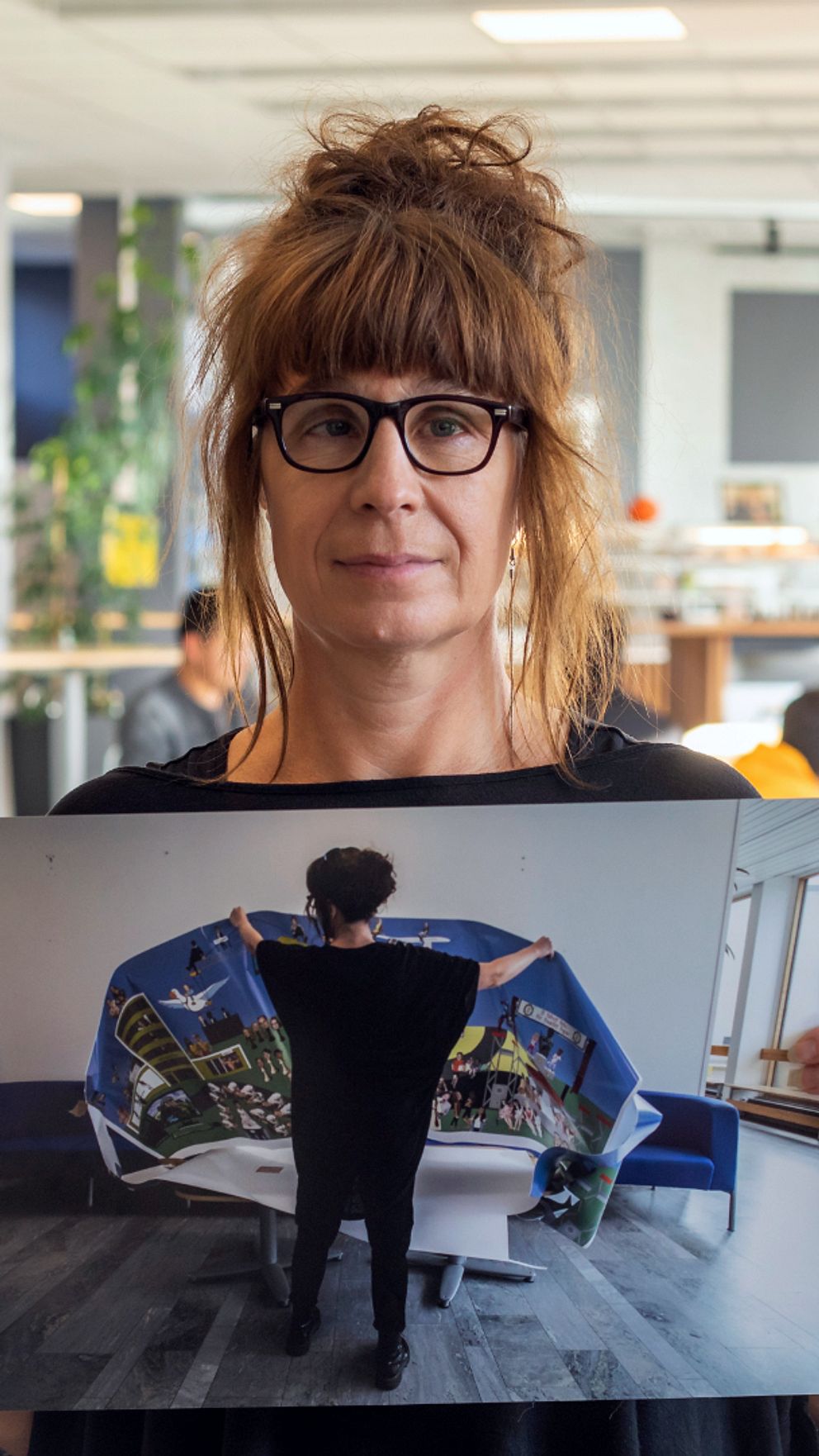 Kvinna i skolmiljö håller upp bild på en kvinna om håller i en affisch