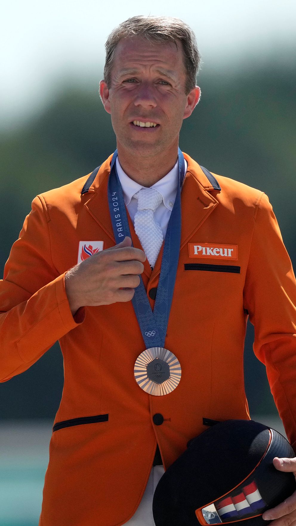 Person i orange kavaj med medalj runt halsen och ridhjälm i handen.