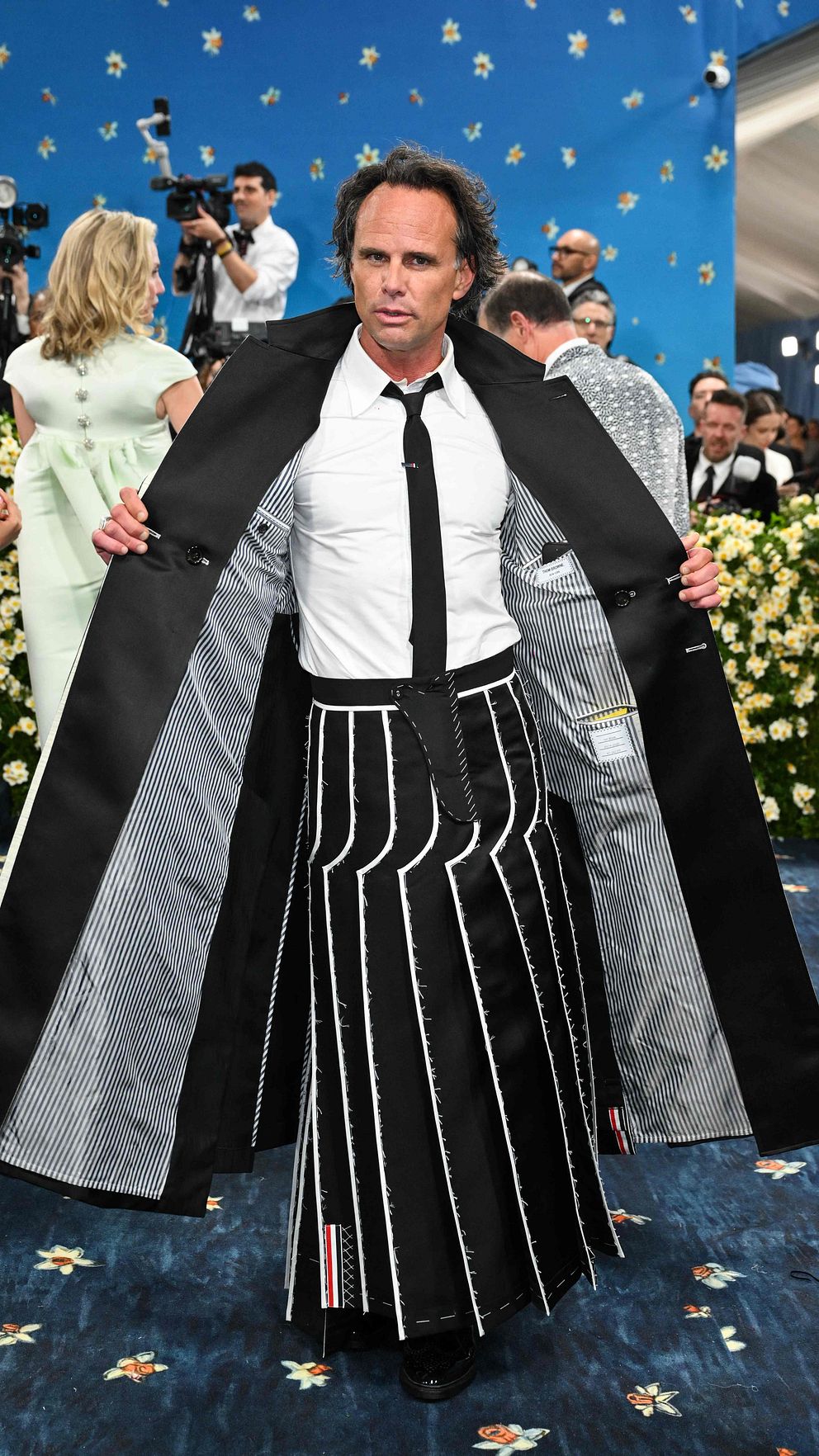 En person visar upp sin rock och randiga kjol på en blå matta omgiven av fotografer.