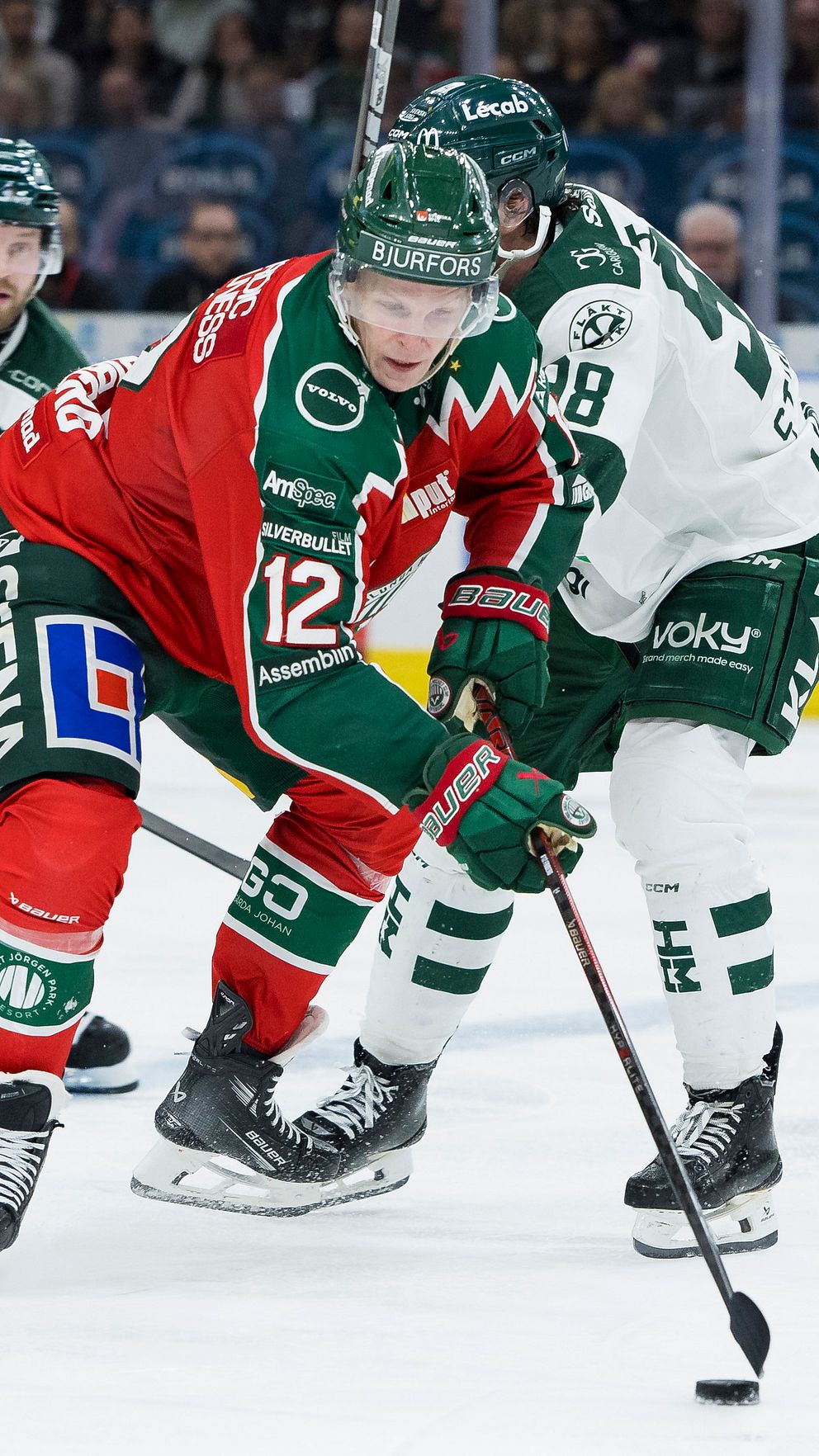 Ishockeyspelare i kamp om pucken under en match på isrink.
