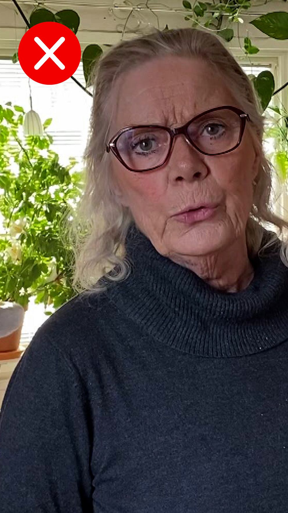 Person i stickad tröja framför grönskande växter inomhus. Rött kryss i bildens övre hörn.