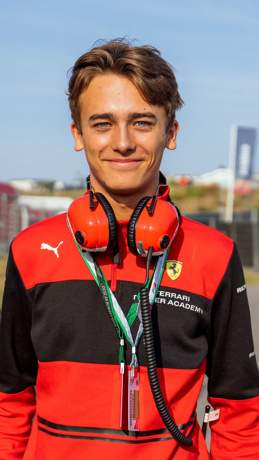 En person i Ferrari-kläder med hörselskydd står utomhus nära pit-lane.