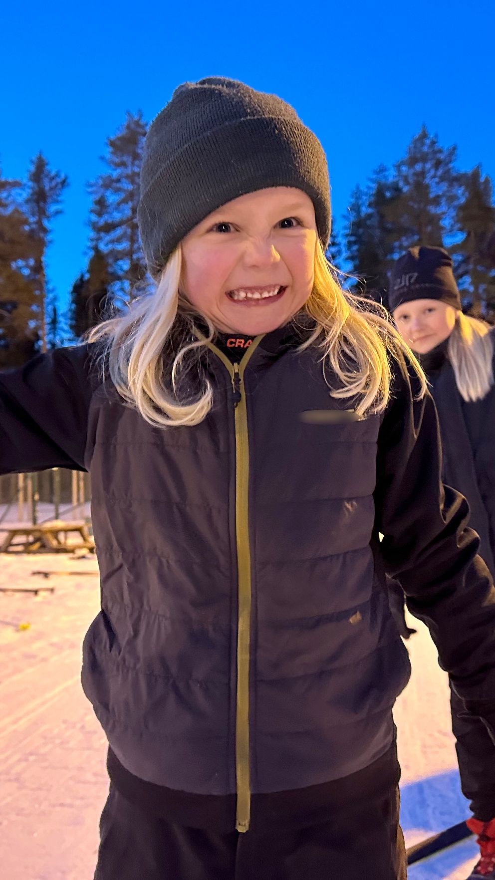 Barn på skidträning visar musklerna och grimaserar till kameran. Kväll i vinterlandskap.
