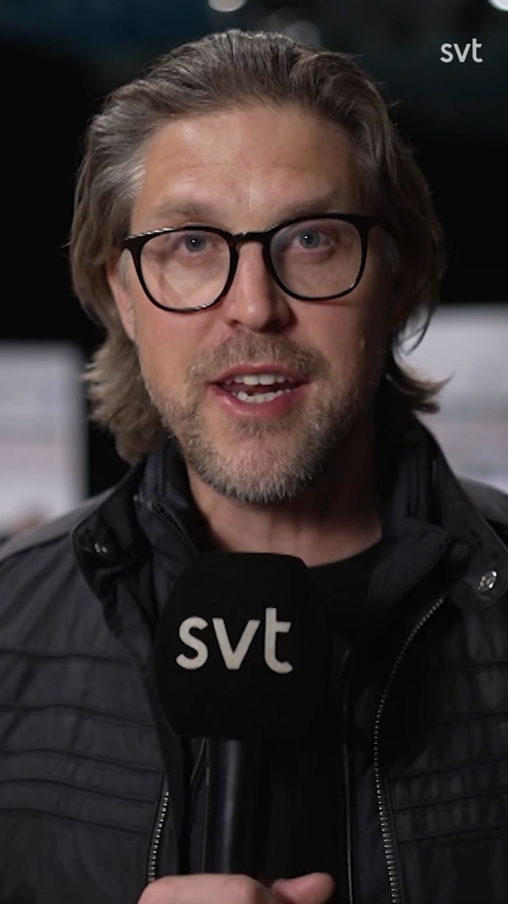En reporter håller en mikrofon med SVT-loggan i studiomiljö.