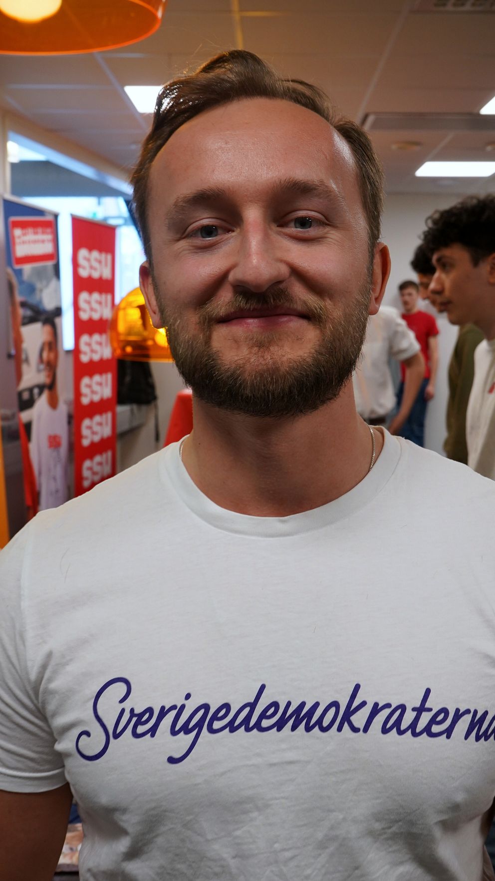 Ung man med kort skägg och kort hår tittar in i kameran.
