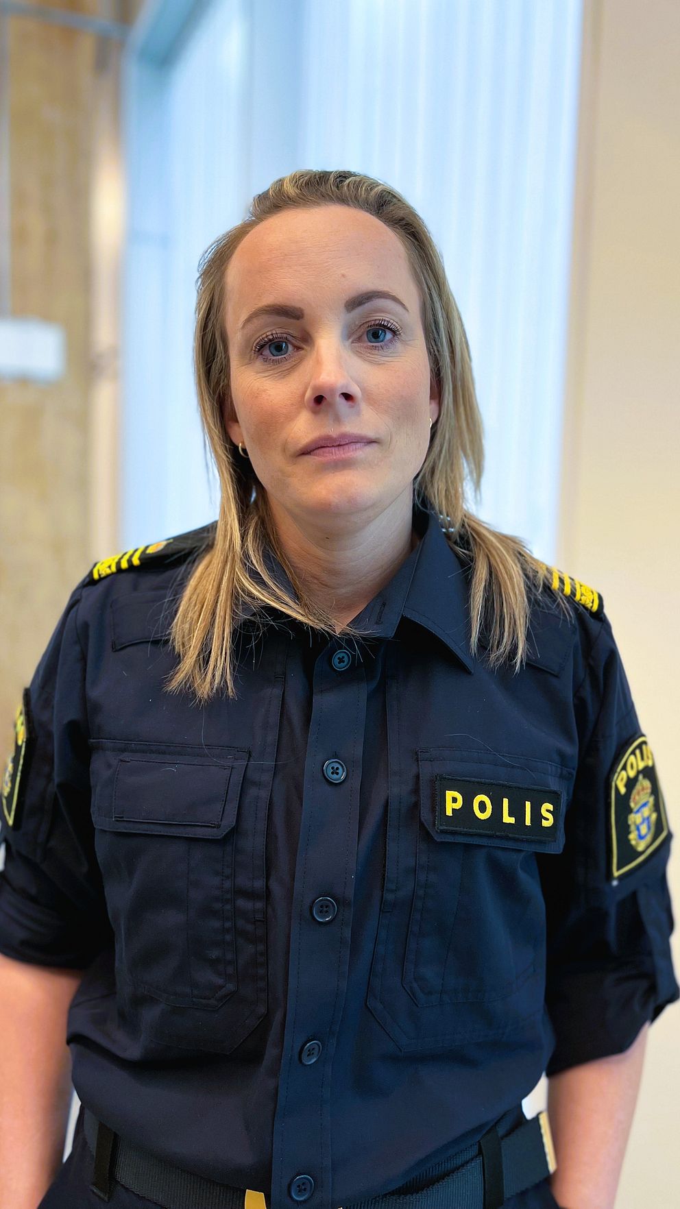 Svensk polis i uniform står inomhus med suddig bakgrund.