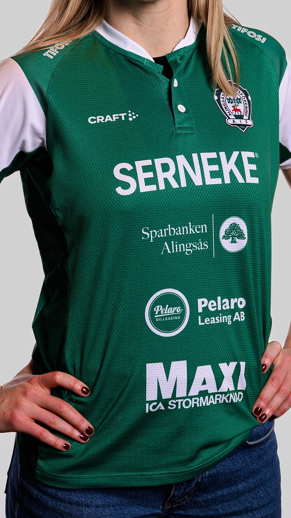 Person i grön idrottströja med sponsorer, händerna på höfterna.