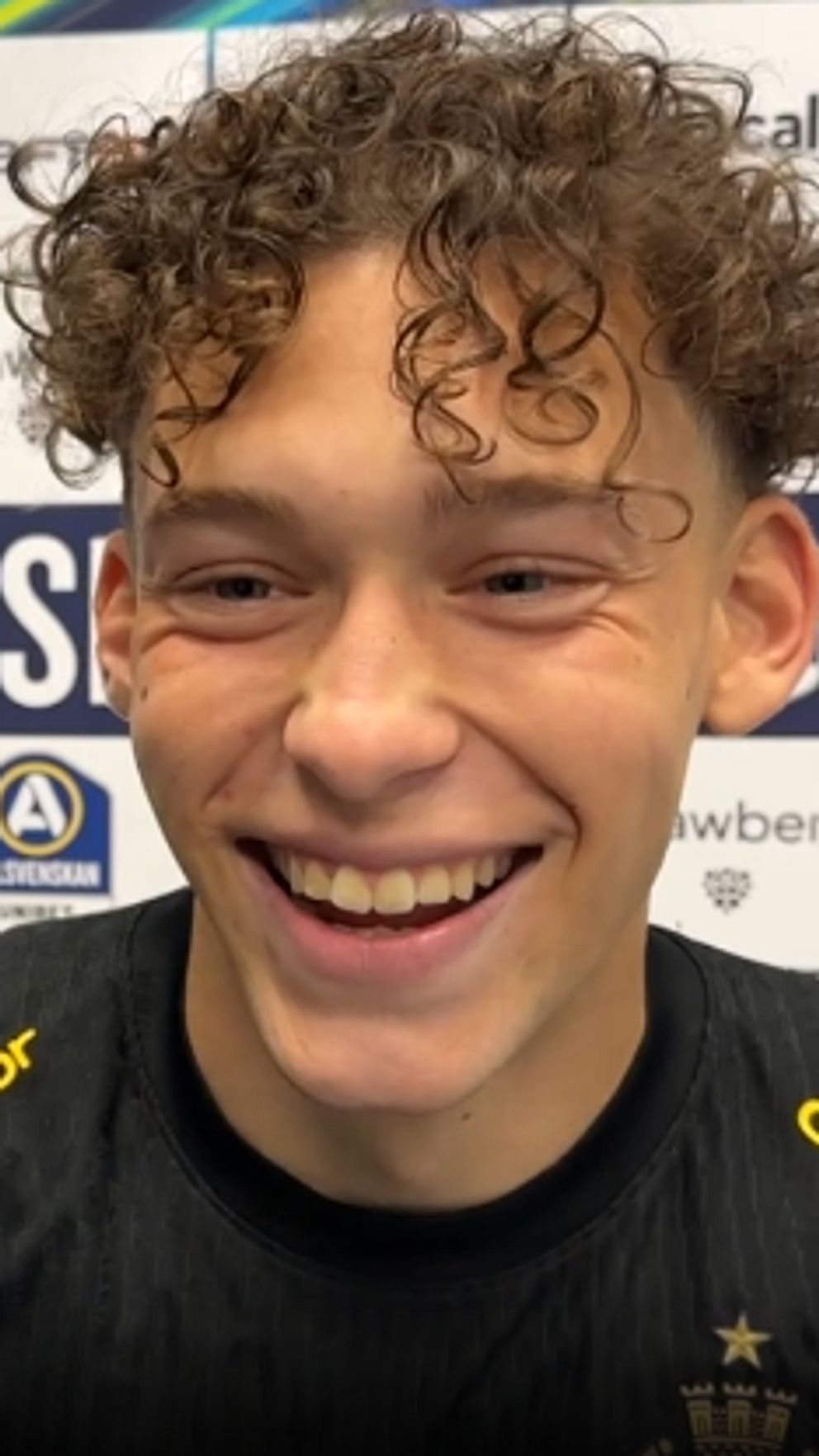 AIK-spelare i svart tröja framför sponsorvägg på presskonferens.
