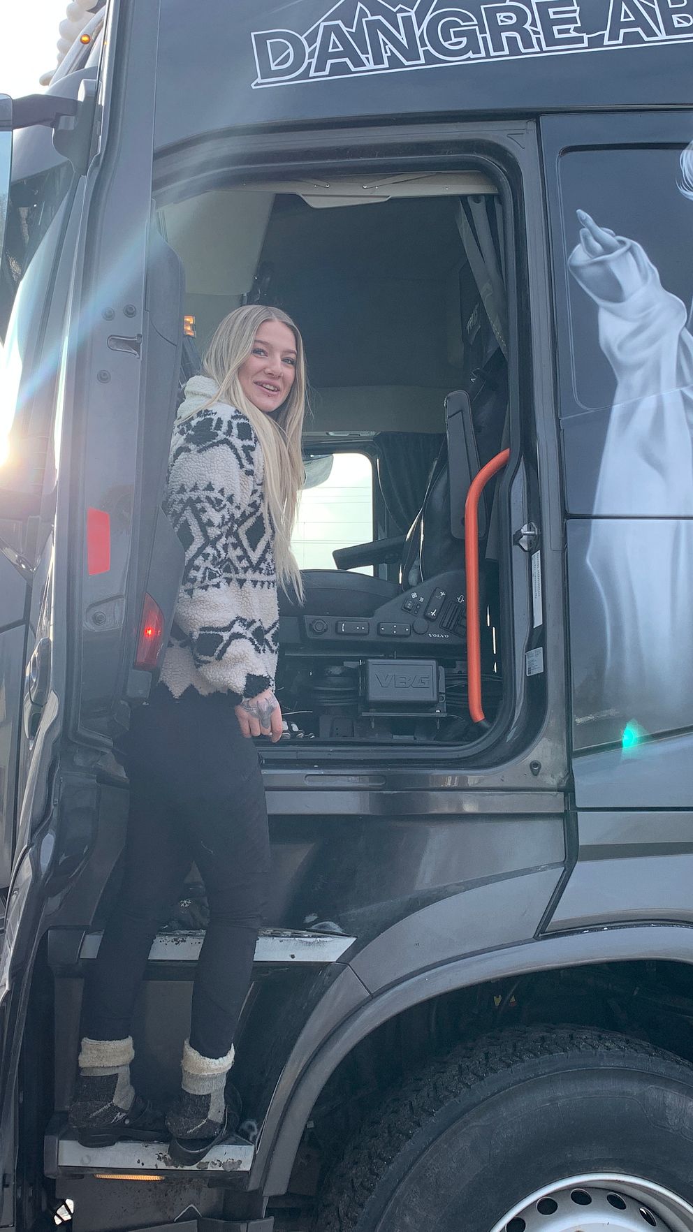 Kvinna kliver in i lastbil med konstnärligt porträtt på sidan. Solen skiner.
