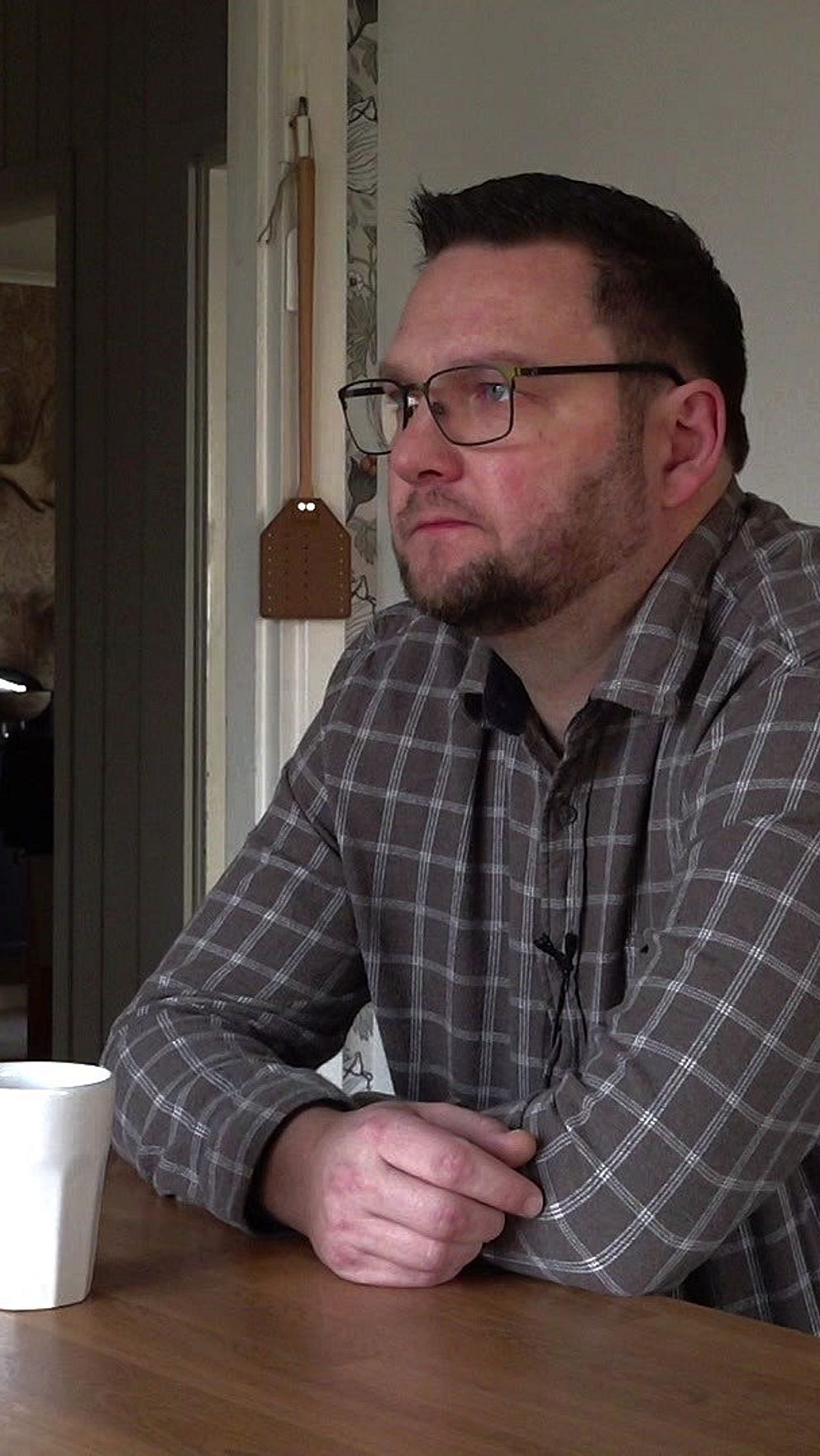 Man sitter vid köksbord med en kopp, omgiven av lantlig inredning.