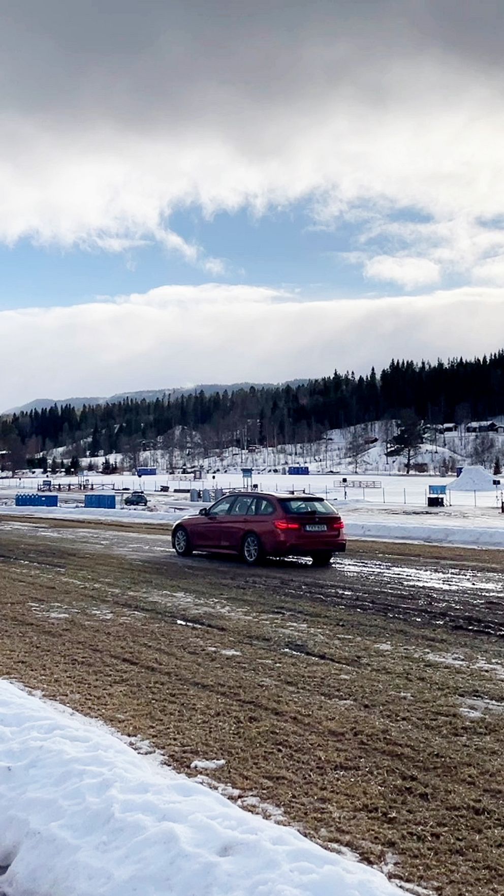 Bilar kör på en lerig väg i ett vintrigt landskap. Moln täcker himlen delvis.