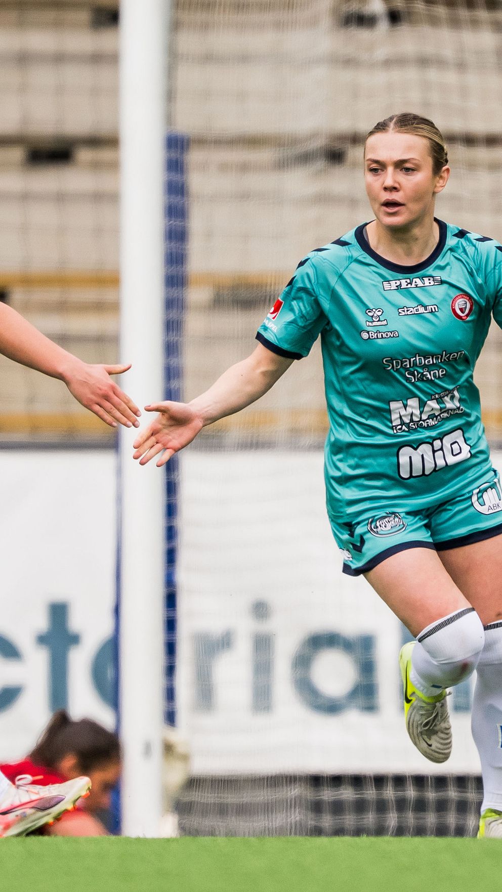 Två fotbollsspelare i gröna dräkter ger varandra en high five under match.