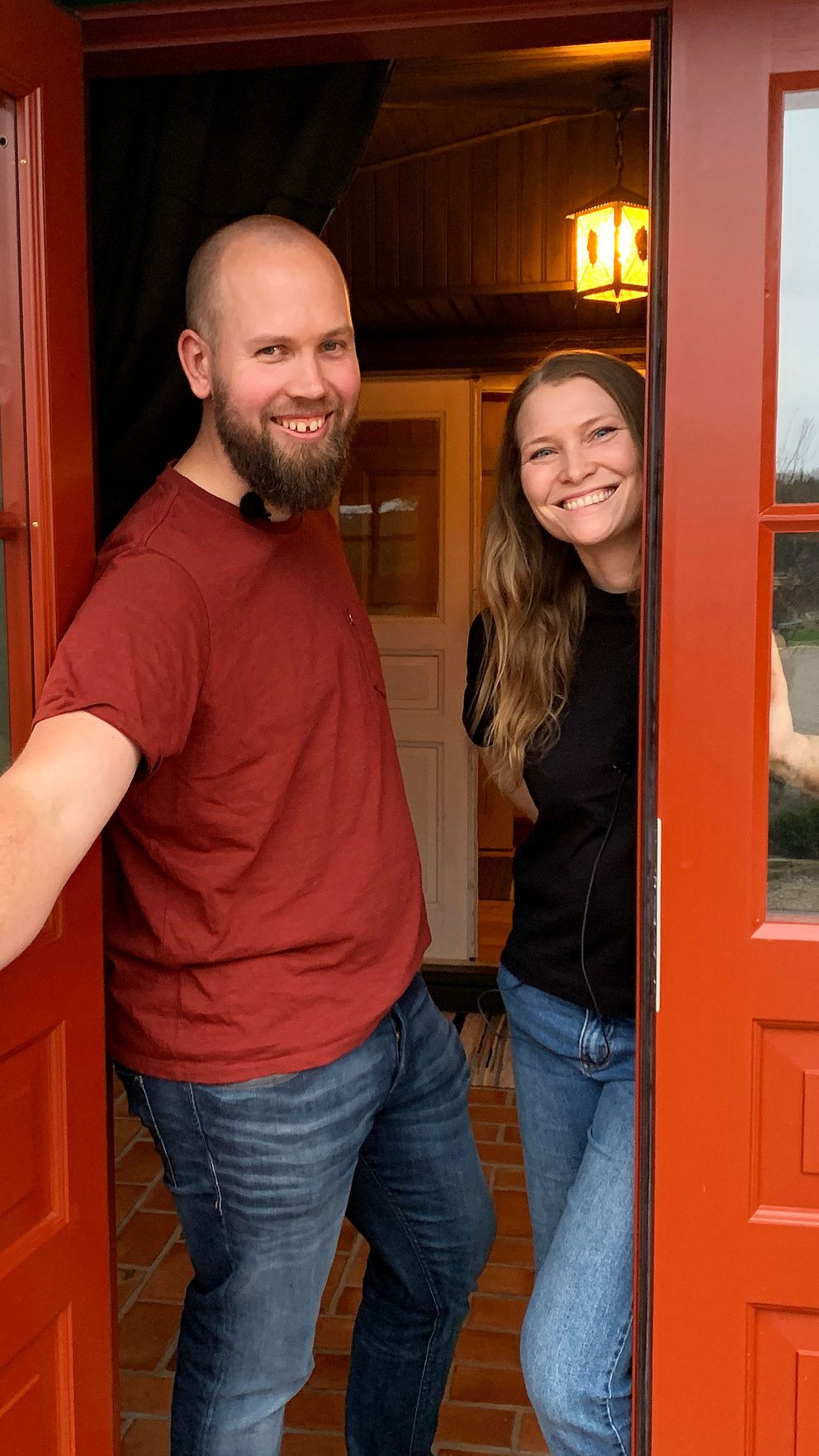 Marcus Antonsson Jonsson öppnar leendes den röda dörren till sitt hem. Bakom honom i dörröppningen står sambon Madeleine Johansson.