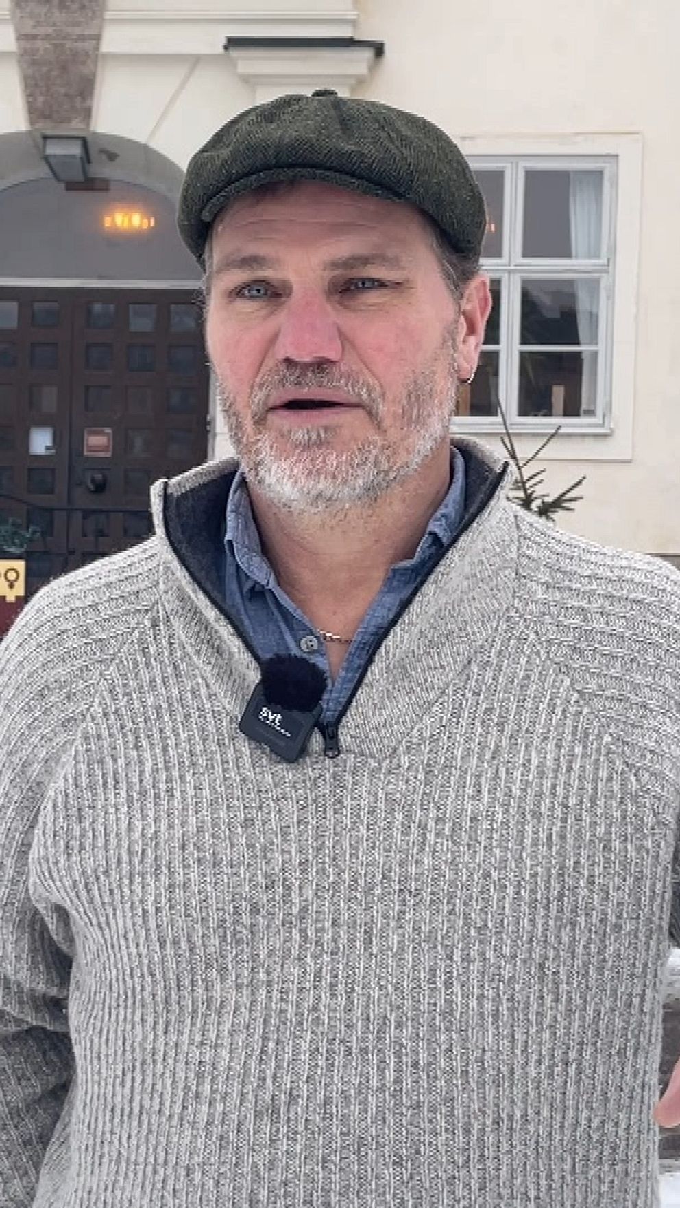 Socialdemokraten Jonas Sallén Lennerthson som är ordförande för barn- och utbildningsnämnden i Falu kommun står framför rådhuset som är en äldre byggnad med vit fasad, trappa och trädörr. Marken är täckt med snö och några barrträd syns vid sidan av. Personen bär en stickad grå tröja och en mörk keps.