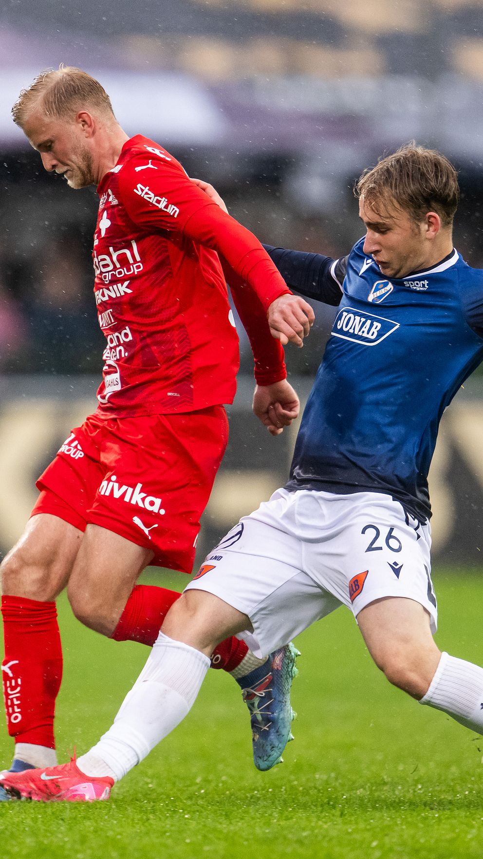 Två fotbollsspelare tävlar om bollen under en match på gräsplan.