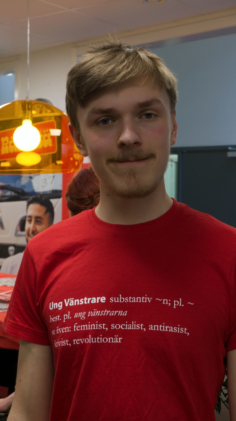 Ung man i mustasch tittar in i kameran