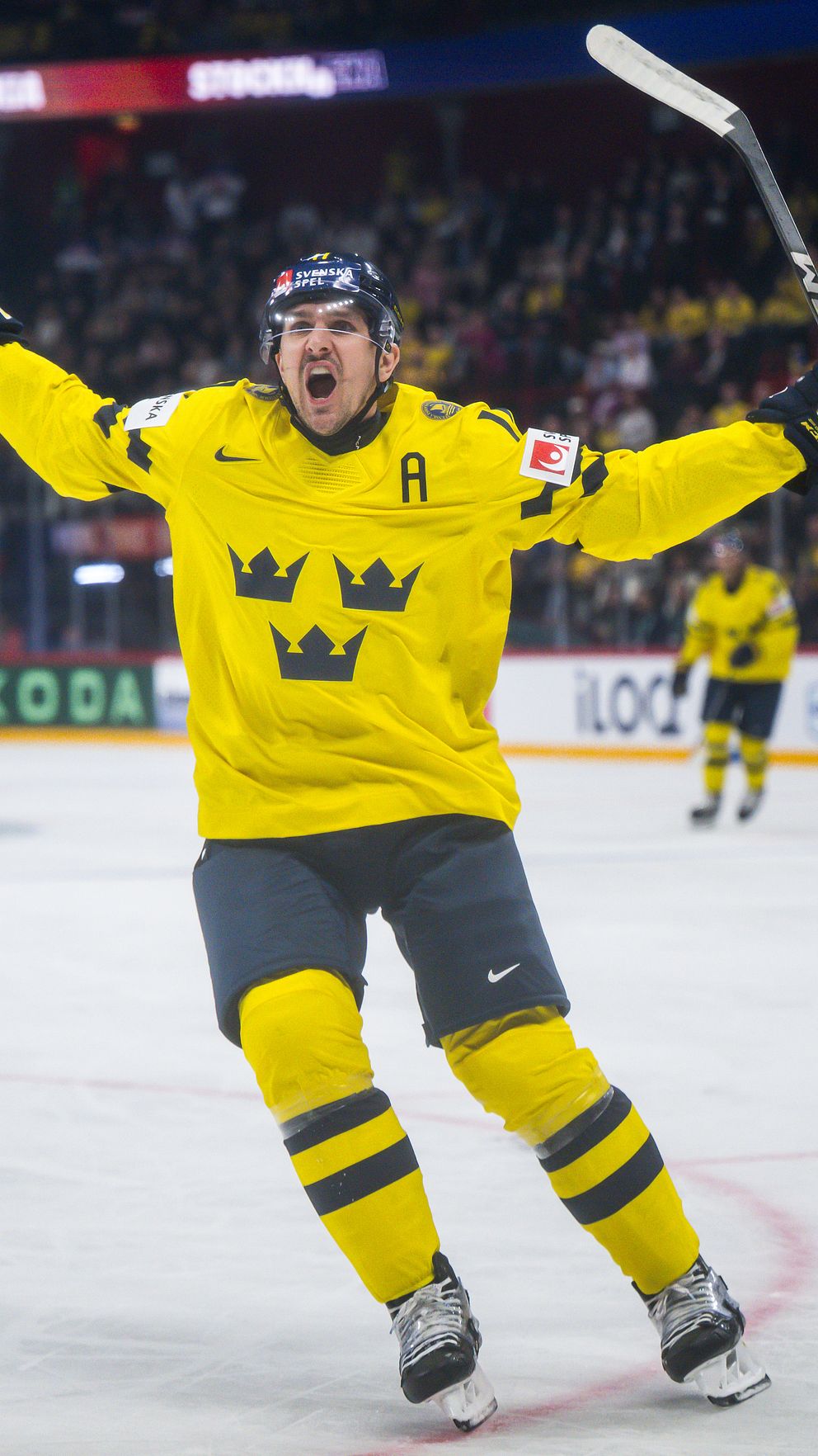 Ishockeyspelare i Tre Kronor-tröja firar mål på isen inför jublande publik.