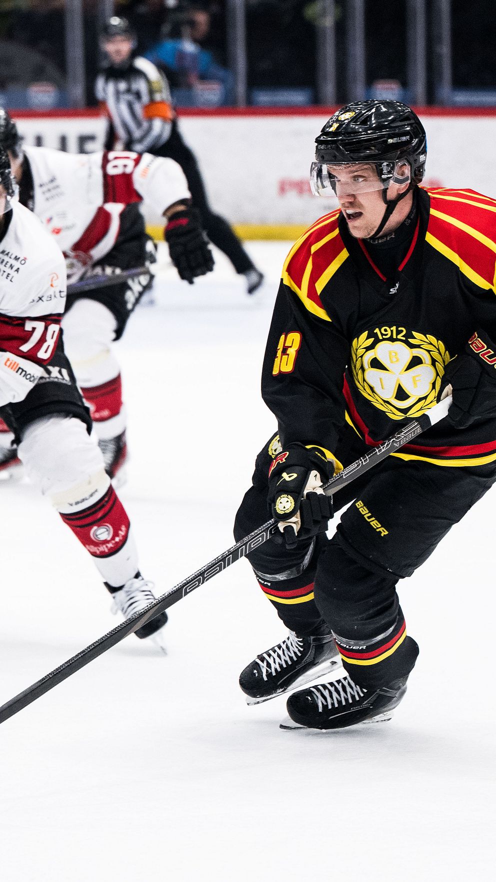 Två ishockeyspelare jagar pucken på isen under en match.