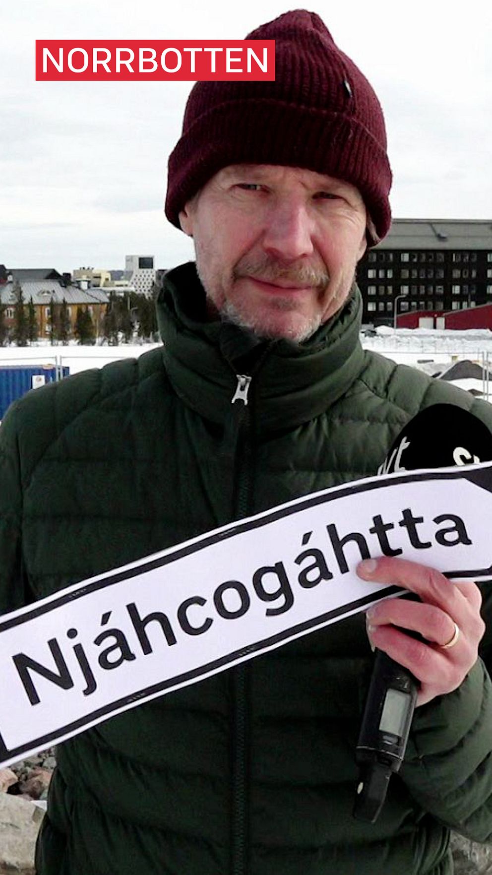 Person håller skylt med texten ”Njáhcogáhtta”. Bakgrund med snötäckt landskap.