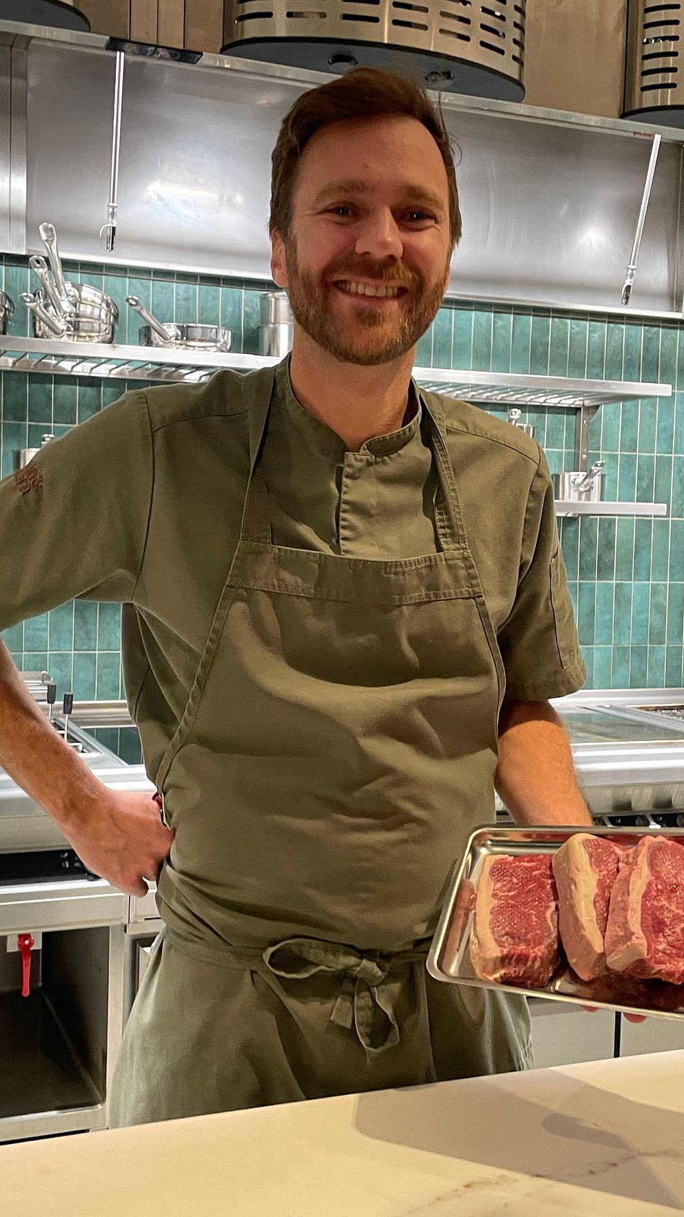Kock i restaurangkök håller tre råa köttbitar på en metallplåt.