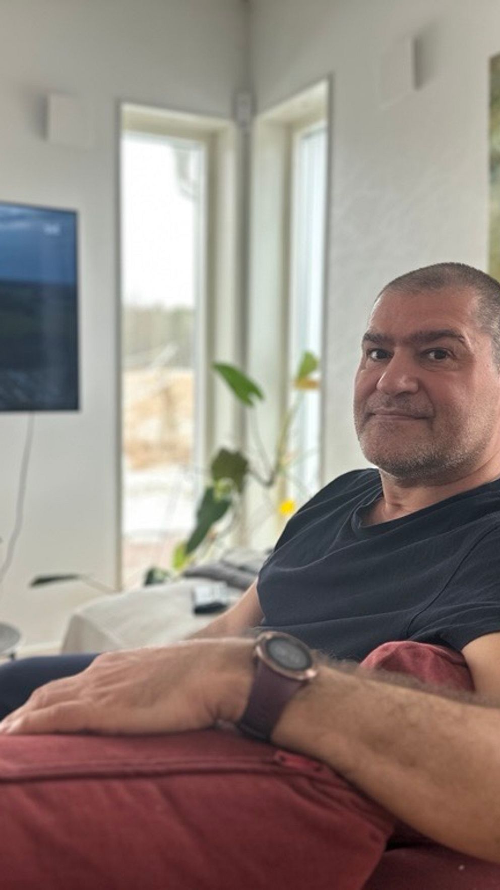 Man sitter på en soffa framför en stor TV i ett ljust vardagsrum. han har postcovid