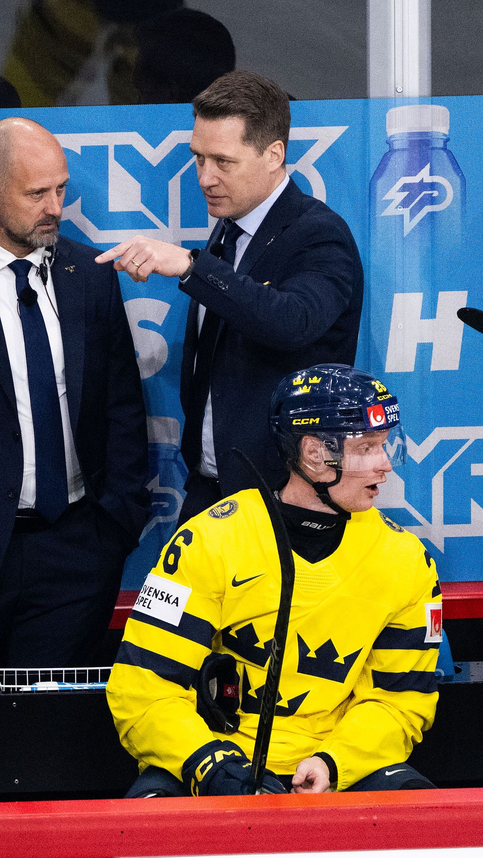 Svenska hockeyspelare och tränare i gula tröjor vid båset under en match.