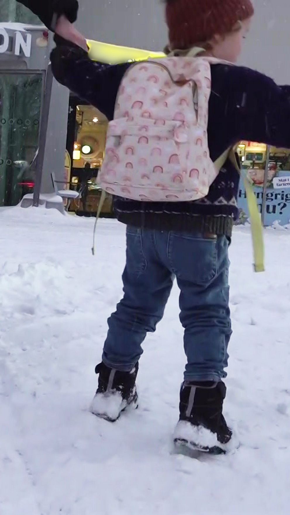 Ett barn drar i handen på en vuxens medan de går genom snön med en barnvagn.