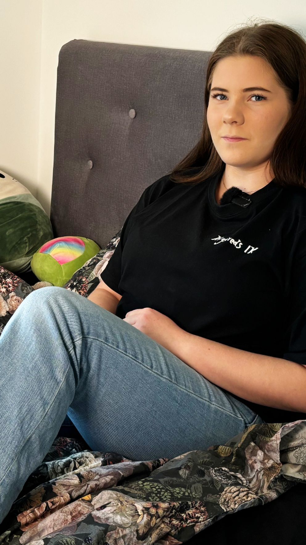 Tjej sitter på en säng i ett sovrum, med en nalle som dekoration.