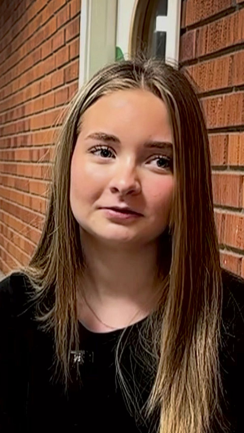 Kvinna sitter på bänk i en korridor. Två personer går bortåt i bakgrunden.