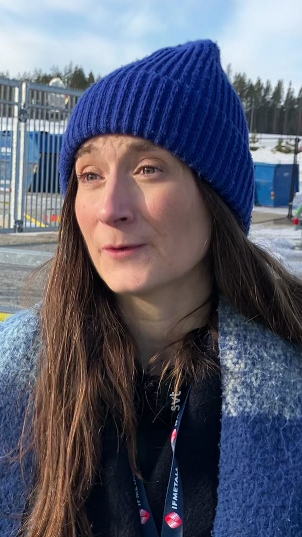 Person i blå mössa framför en industrianläggning på vintern.