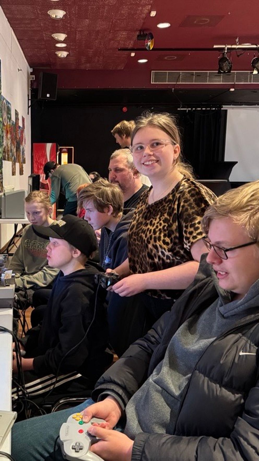 Ungdomar spelar retrospel i ett spelrum med gamla TV-apparater och affischer på väggarna.
