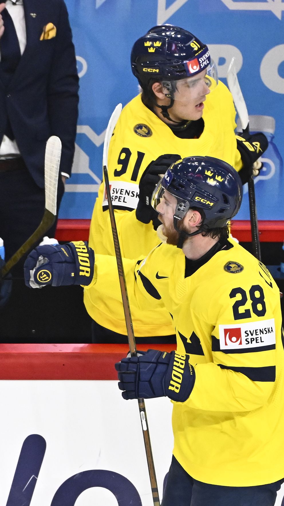 Ishockeyspelare i Tre Kronors gula tröjor firar vid båset under match.