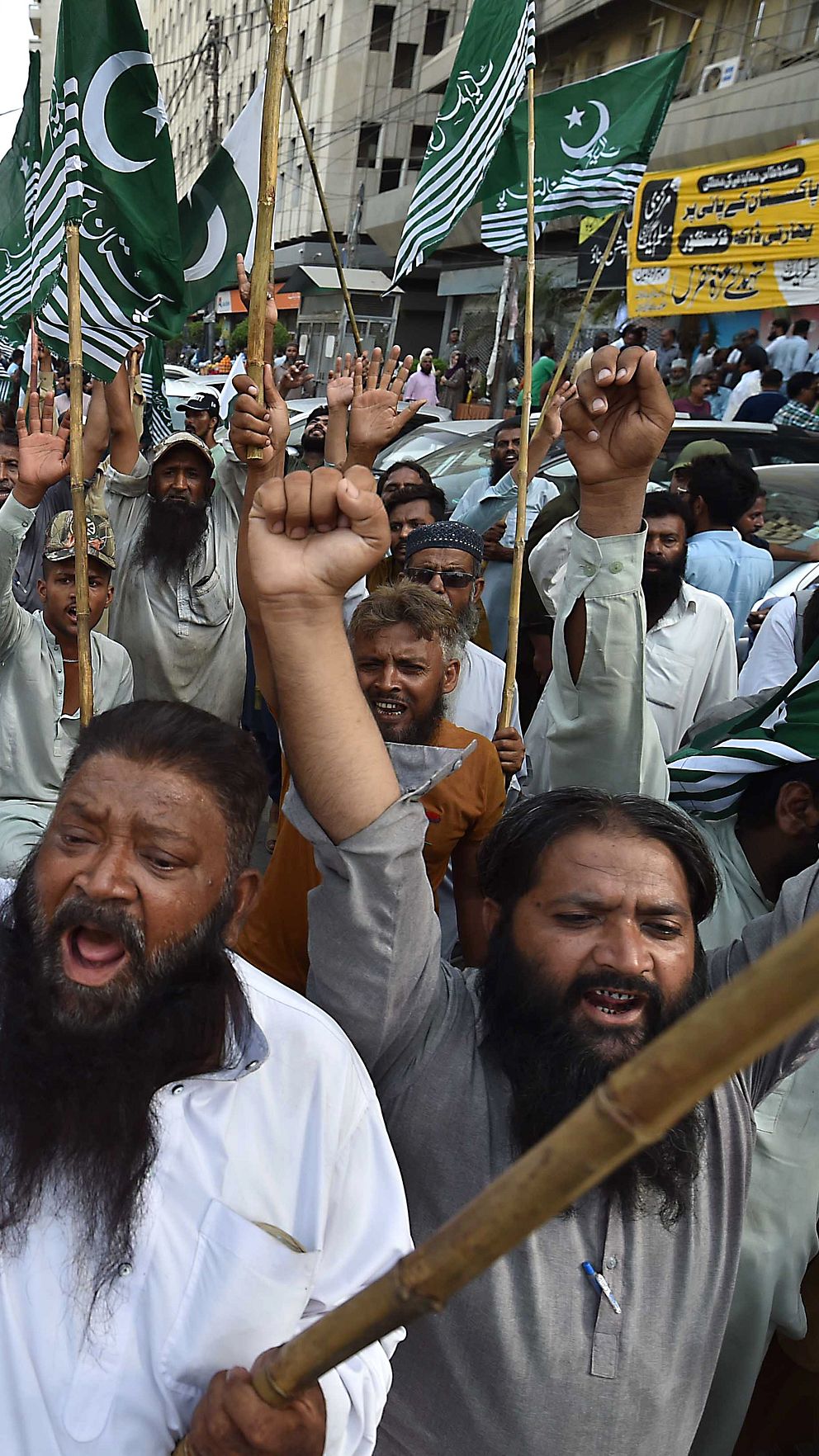 Demonstranter med pakistanska flaggor samlas och håller upp händerna i protest.