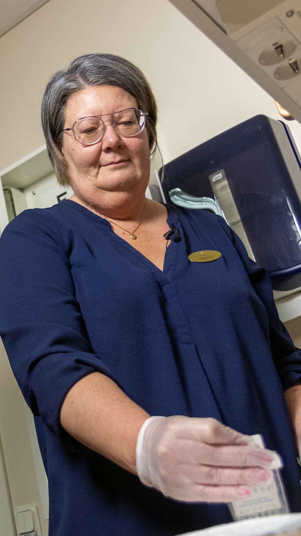 En ung man står i ett rum medan en skolsköterska i sjukhusuniform förbereder ett urinprov för ett drogtest.