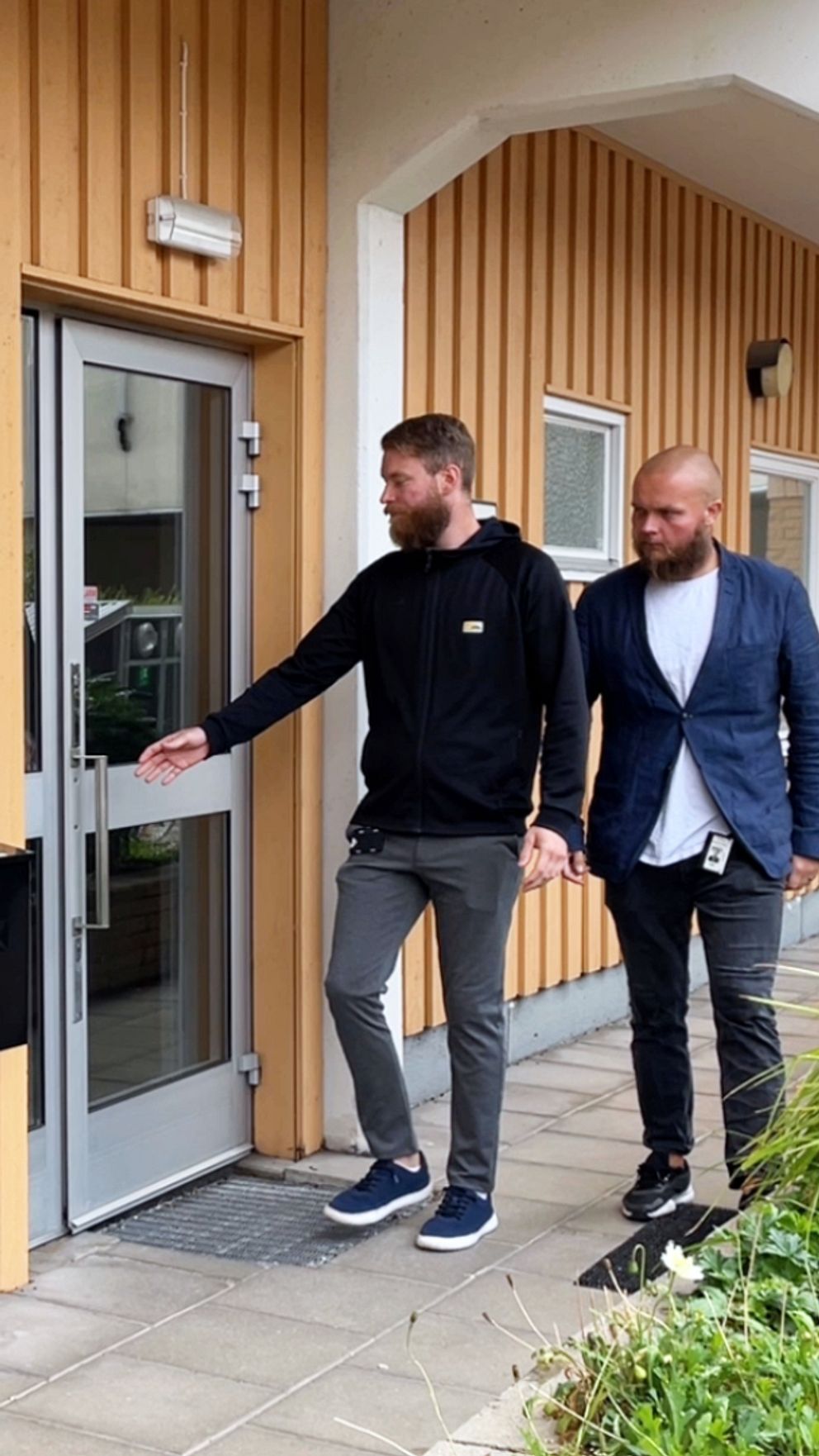 två män vid en gul husfasad som öppnar en dörr