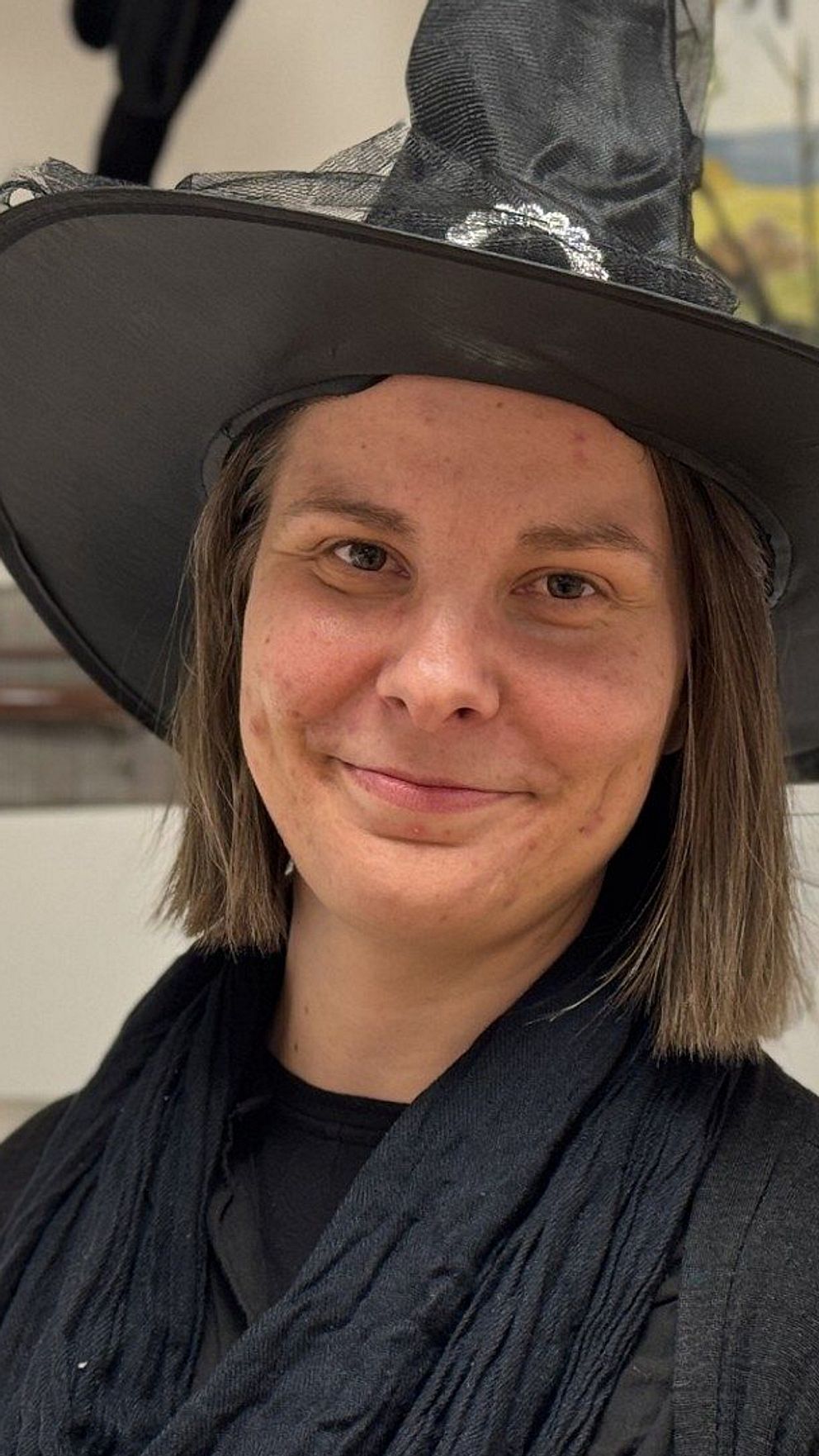 En delad bild som visar en skylt med texten ”Perrong 9¾” och ”Kråkboet” placerad på en trästolpe. Till höger står en person klädd i svart och i en stor häxhatt, omgiven av en lekfull och festlig atmosfär.