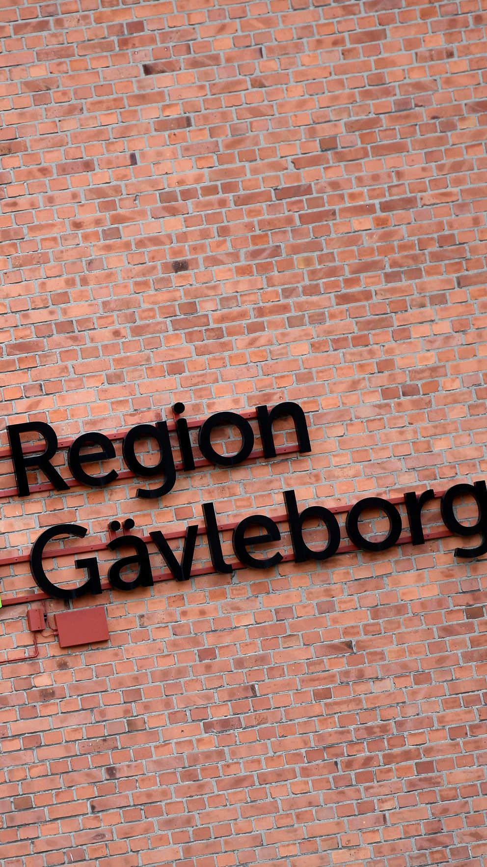 Region Gävleborgs logga på en röd tegelvägg vid ett fönster.