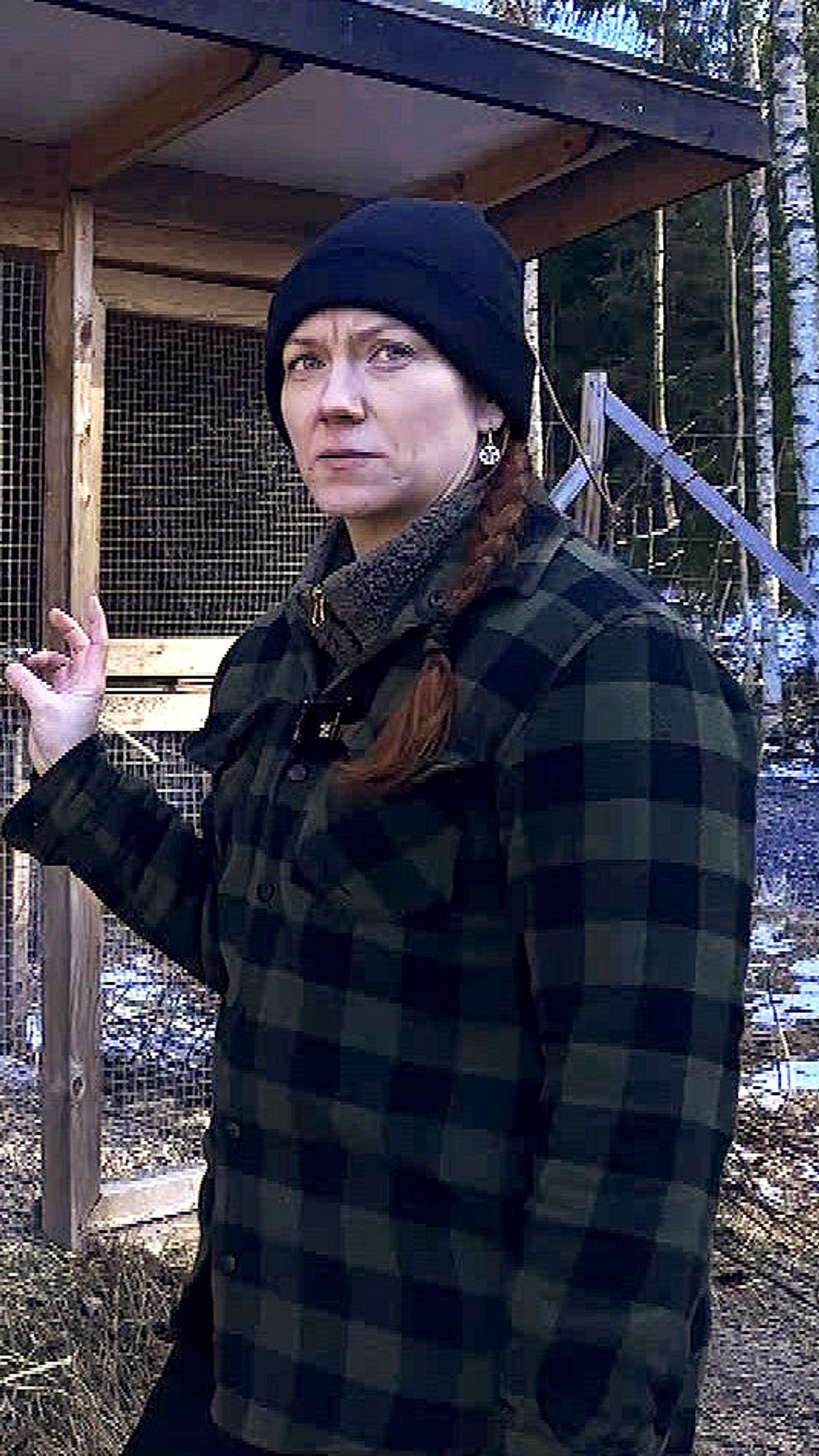 Person i rutig skjorta vid utomhusbur med snötäckt mark i skogsmiljö.
