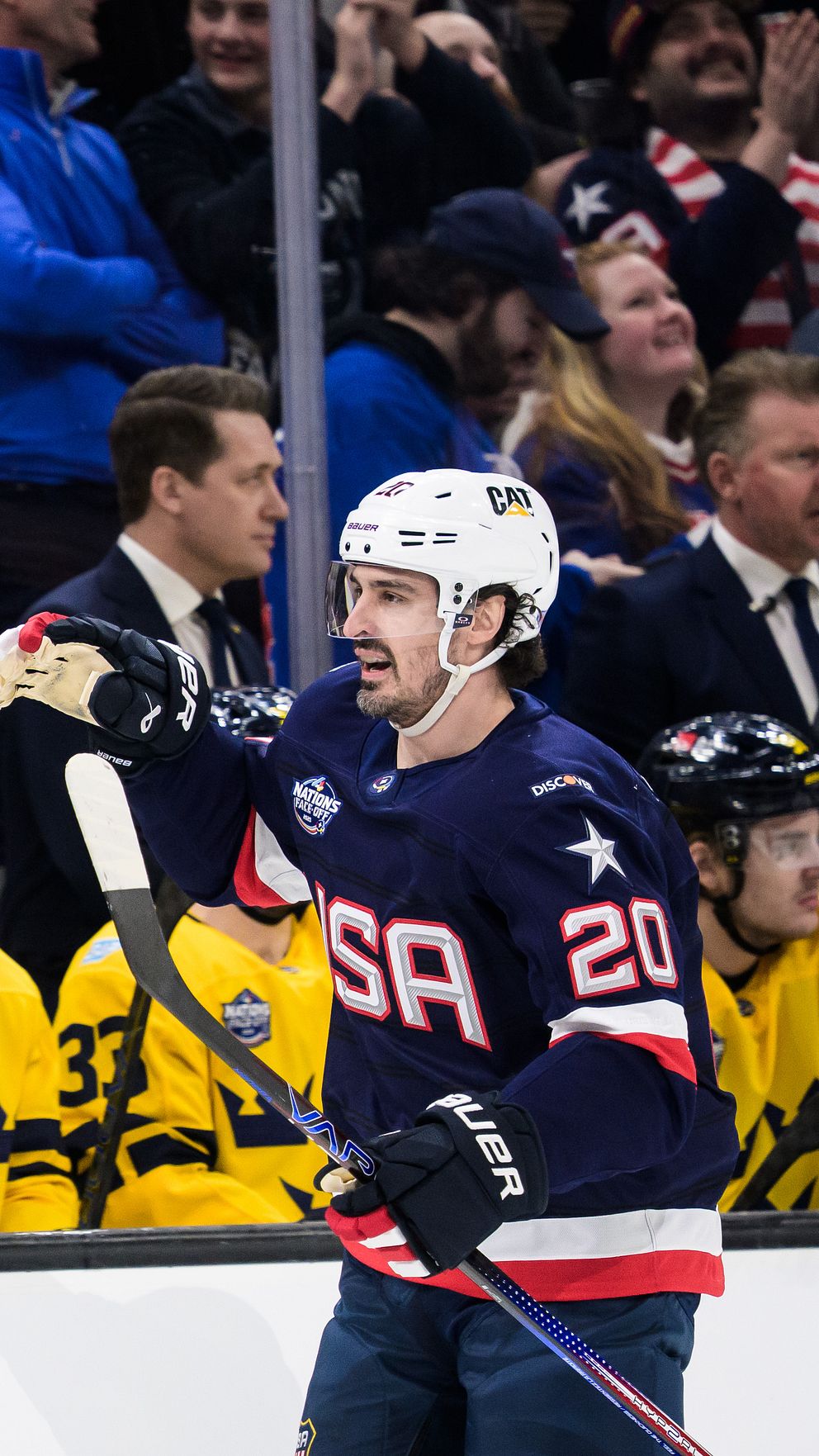 Amerikansk hockeyspelare vid svenska avbytarbänken under match, åskådare i bakgrunden.