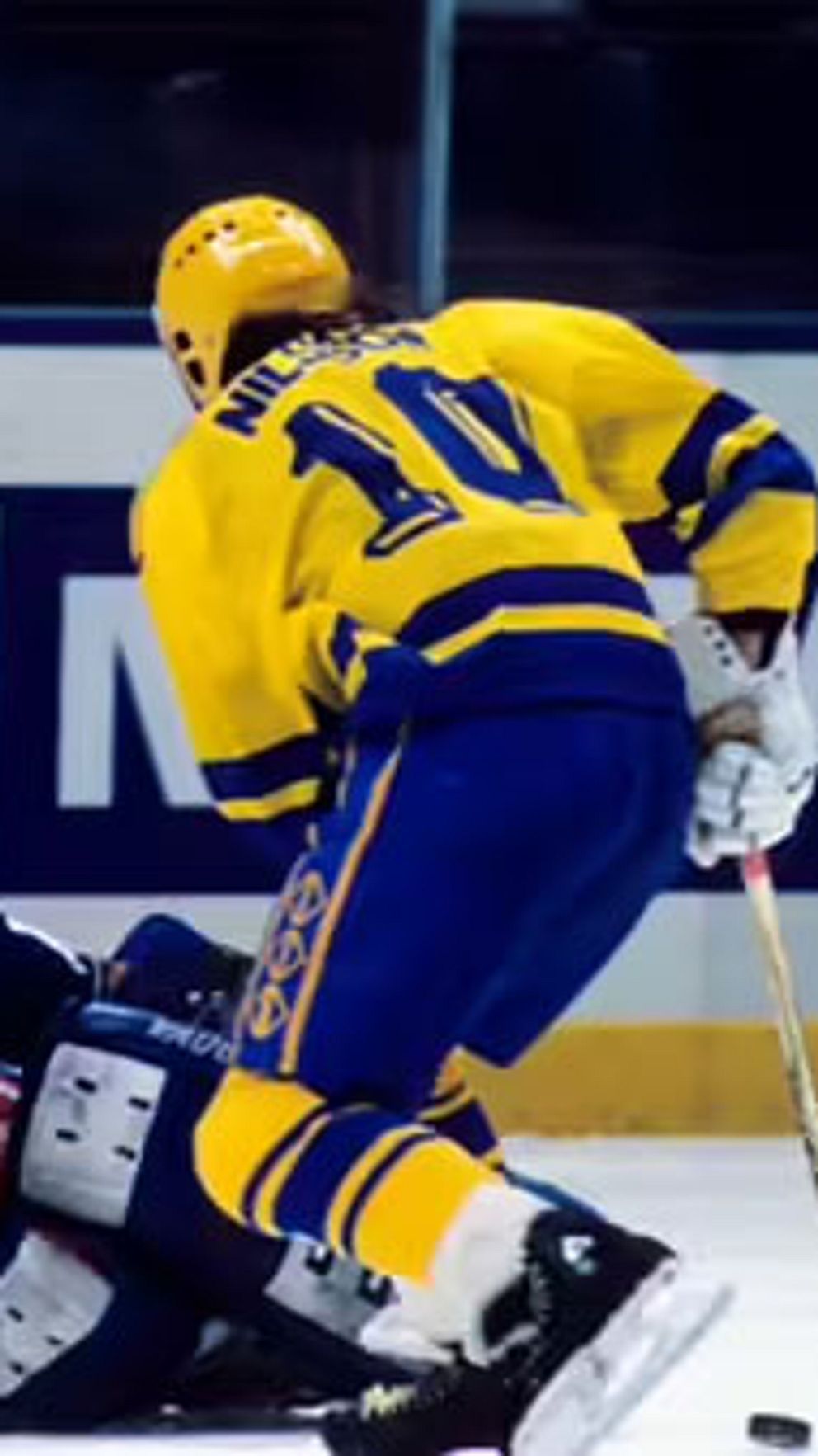Svensk hockeyspelare skjuter mot mål, amerikansk målvakt försöker rädda pucken.