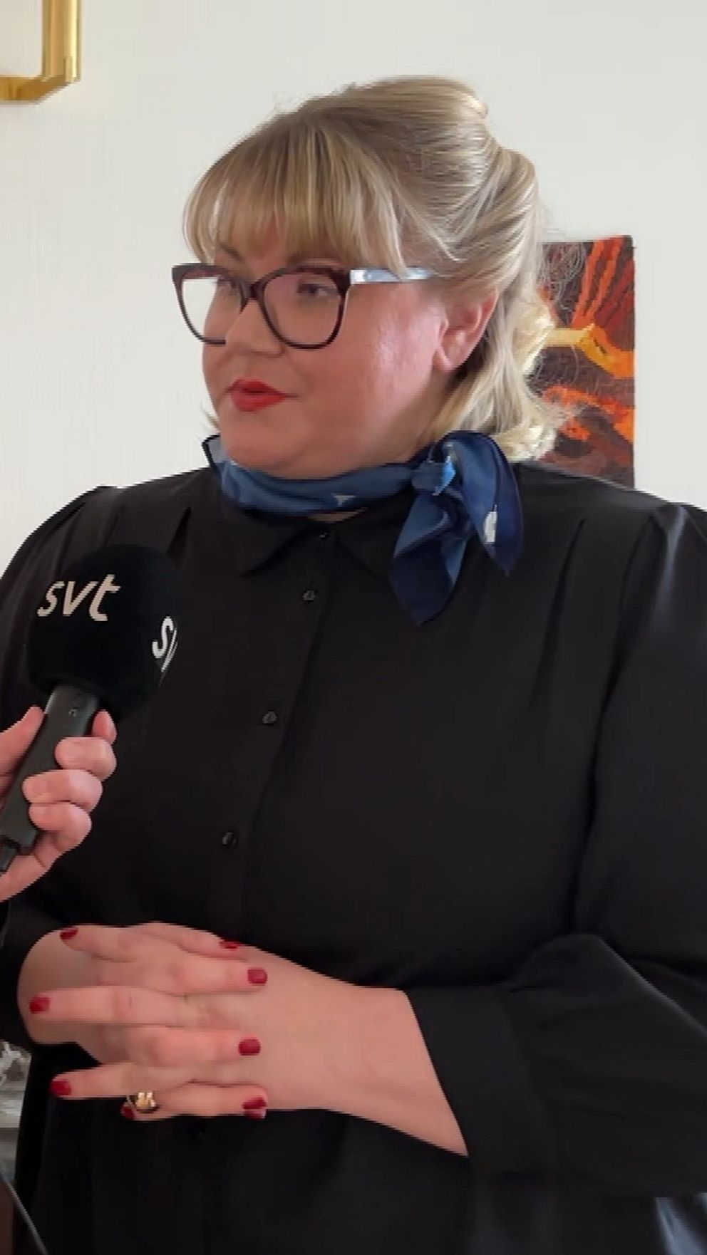 Reporter intervjuar kvinna inomhus med mikrofon märkt SVT.