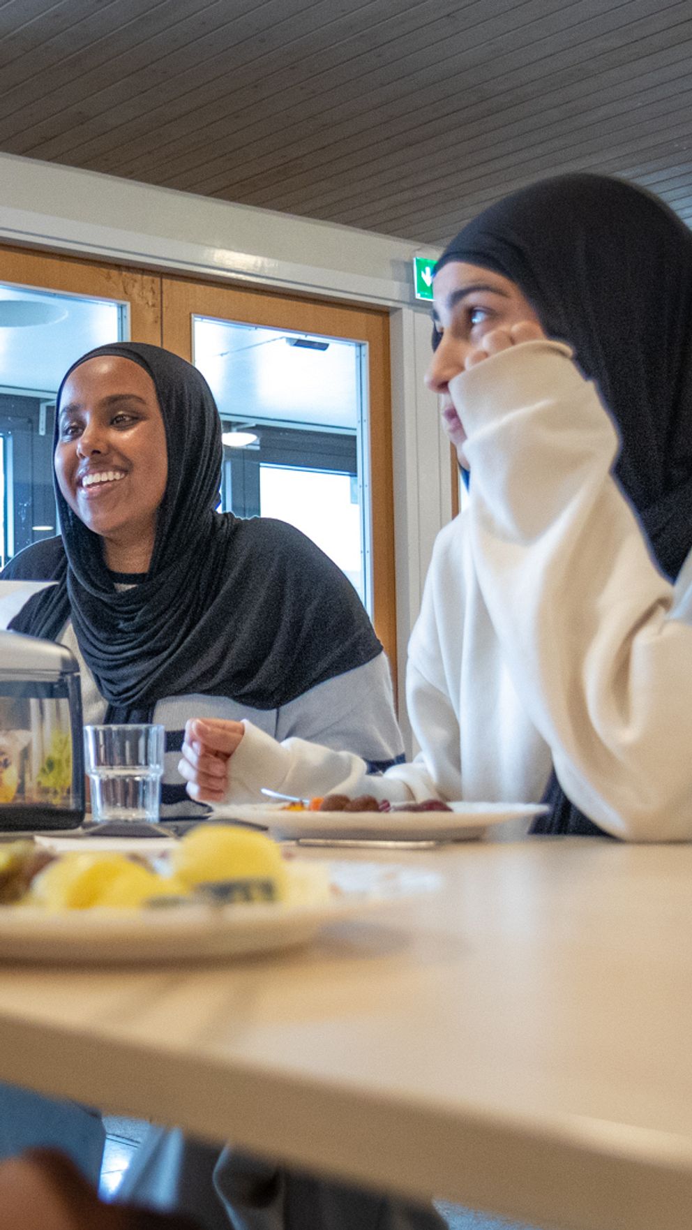 Debatt med flera talare på podium till vänster, och två personer som sitter vid ett bord i en restaurang till höger. På bordet finns mat och dryck.