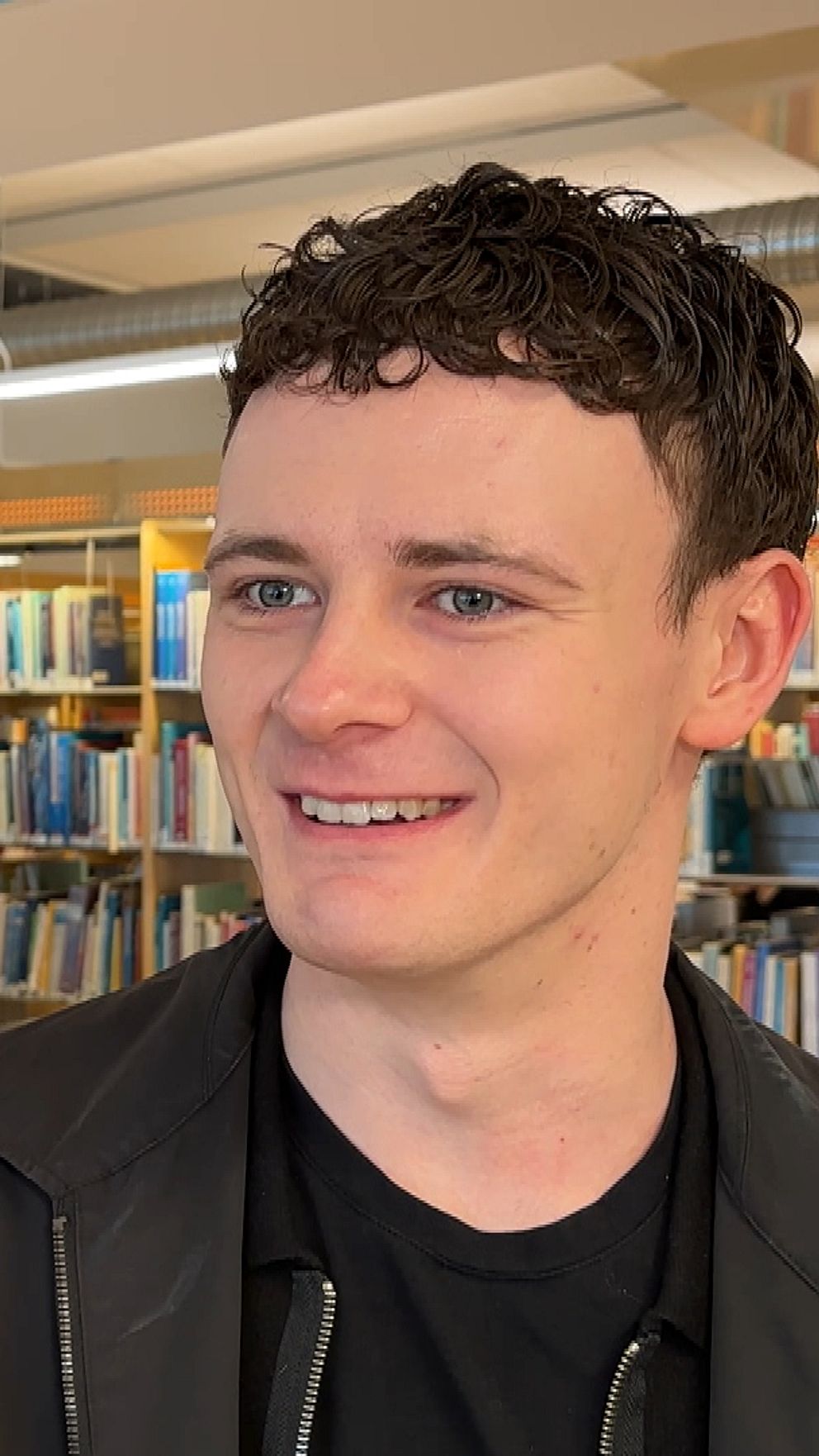 Studenter arbetar vid bord i ett bibliotek, omgivna av bokhyllor.