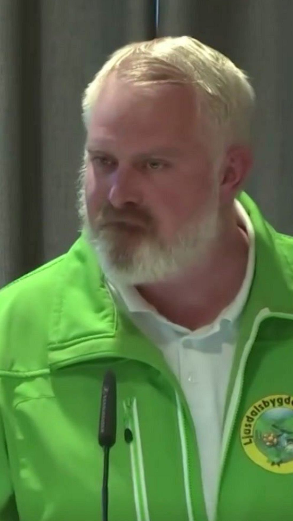 Delad bild. Till vänster talar en kvinna vid mikrofon. Till höger man i grön jacka vid talarstol.