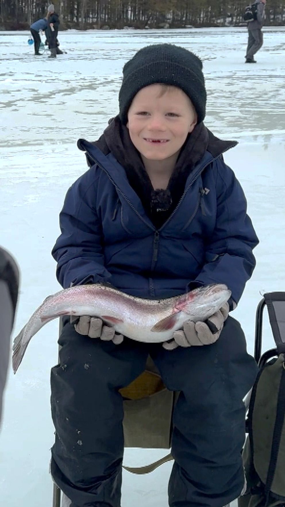 Tre barn som är ute på en isig sjö och fiskar. två av dom håller i fångsten: fiskar
