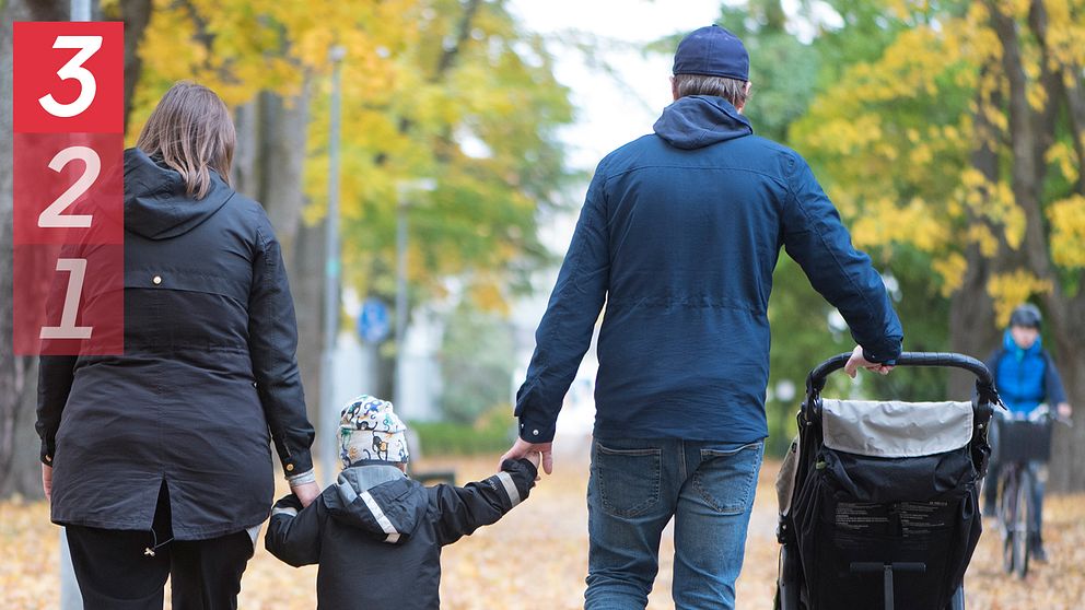 En familj går hand i hand längs en höstfärgad väg. En vuxen kvinna och en man som håller en liten flicka i handen, medan de också skjuter en barnvagn. Träden runt omkring har gula och gröna löv, vilket förmedlar en mysig höstkänsla. I övre vänstra hörnet syns siffrorna 3, 2 och 1 i röd färg.