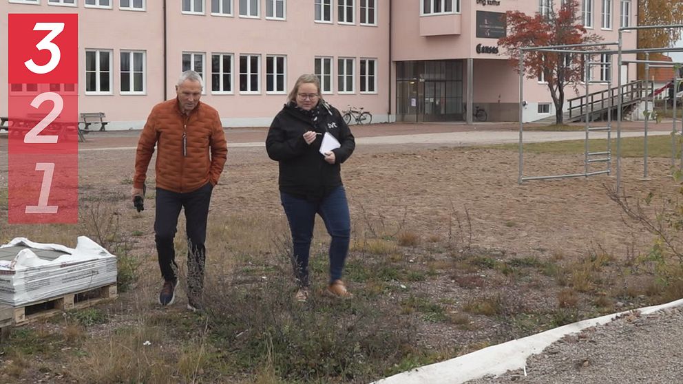 Morabon Ove Hållmarker och SVT:s reporter Ann-Louise Julin går omkring på Strandenområdet i Mora. Det ligger en pall men marksten i gräset och i bakgrunden syns Rosa huset.