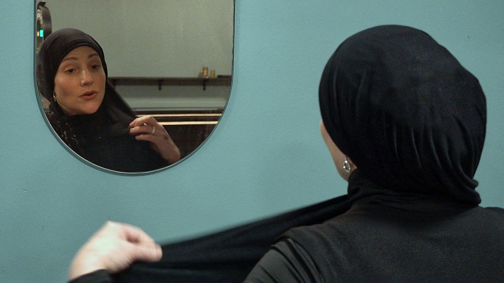 En kvinna sätter på sig en svart bomullsslöja och tittar sig i spegeln.