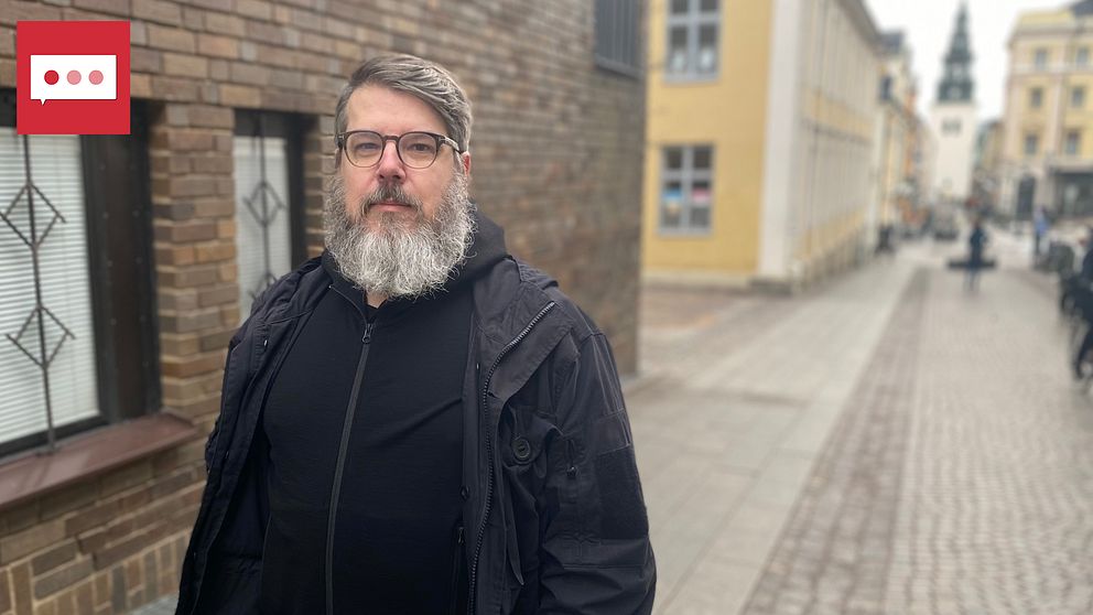 Leif Nixon står på en gågata i Linköping i svarta kläder med sankt larskyrkan i bakgrunden.